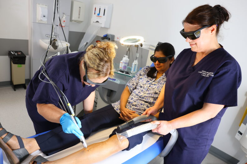 Two nurses carrying out a laser treatment on a woman's leg