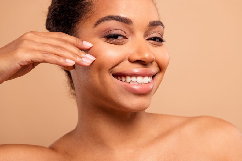 Image of young woman smiling and touching her cheek.