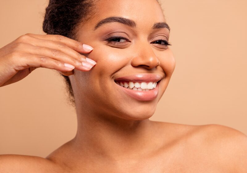 Image of young woman smiling and touching her cheek.